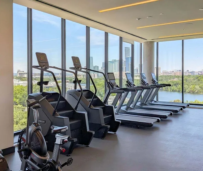 Modern fitness center with state-of-the-art treadmills and climbers, overlooking a scenic city skyline and river view through floor-to-ceiling windows.
