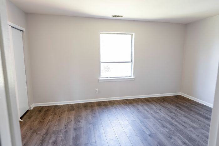 Empty bedroom at Woodcrest Village Apartments with wood-look floors and a central window.