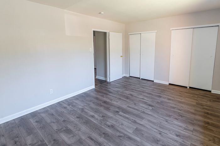 Empty bedroom with gray wood-look floors and two sliding-door closets.