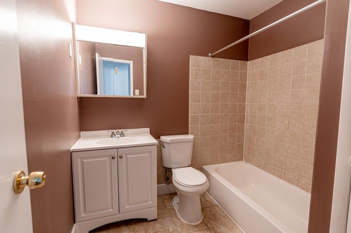 Bathroom with white vanity, mirror, toilet, and tub with beige tile at Woodcrest Village apartments.