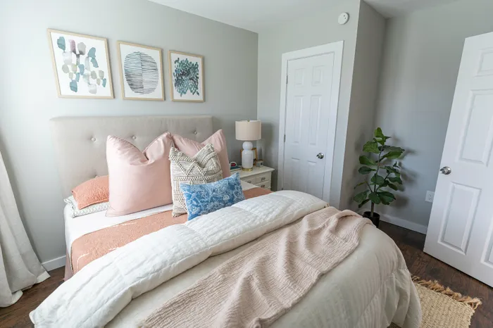 Bright bedroom with tufted headboard, layered bedding, framed artwork and a plant at 405 at Main Apartments.