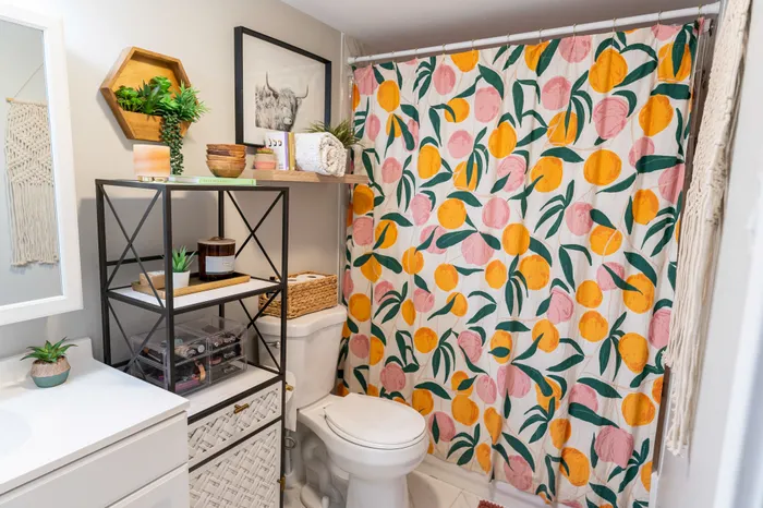Bathroom with a colorful fruit-pattern shower curtain, shelving, and toilet at 405 at Main Apartments.