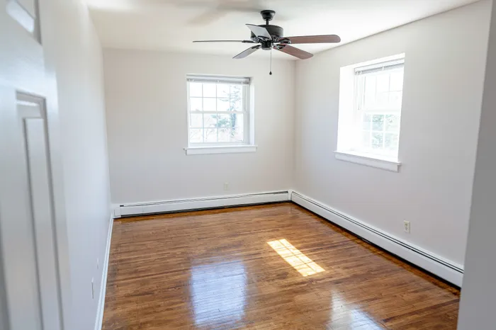 corner room with windows, ceiling fan, and wood floor