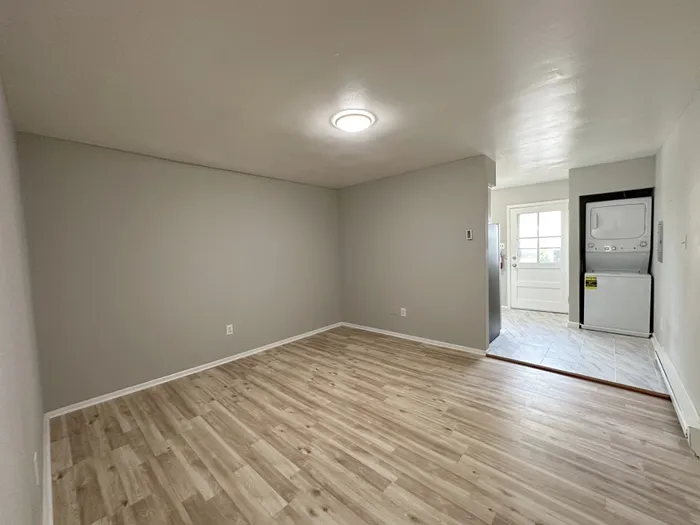 Living area with laminate floors, gray walls and stacked washer/dryer. with washer and dryer