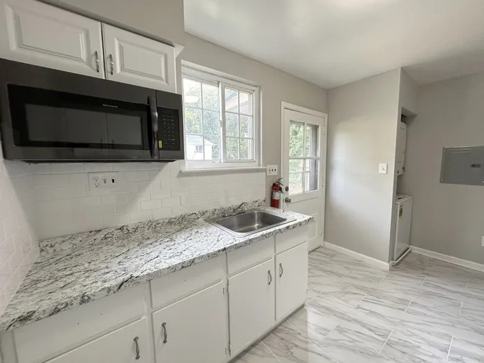 Kitchen with white cabinets, granite countertop, microwave, sink and stacked washer/dryer.