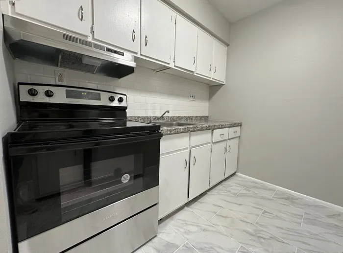 Kitchen with white cabinets, granite countertop, subway tile backsplash and stainless electric range at Woodland Manor.