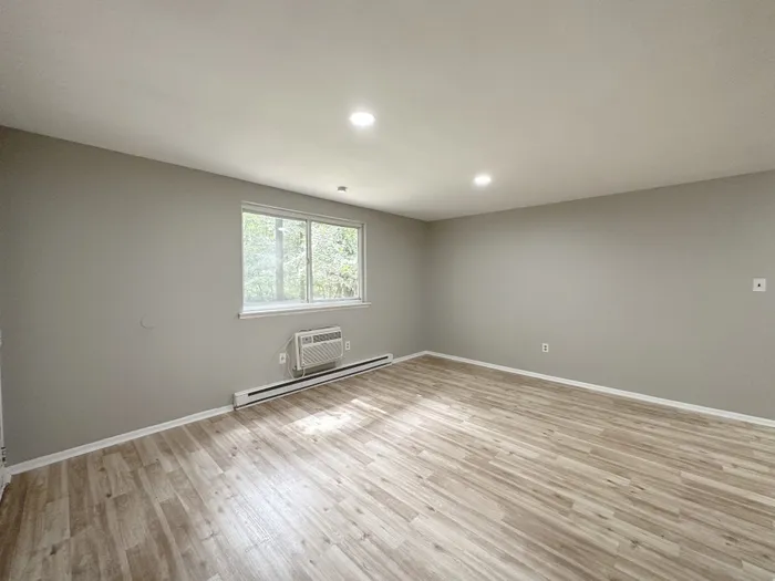 Empty living room at Woodland Manor Apartments in Morrisville, PA with wood‑look floors, gray walls, wall air conditioner