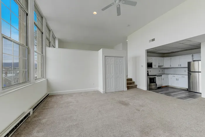 Open-plan living room and kitchen with carpet, large windows, and stainless appliances at Franklin Manor, West Reading.