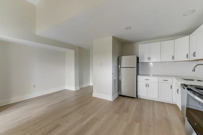 Open-plan living room and kitchen with white cabinets, stainless appliances, and wood floors at Franklin Manor Apartments.