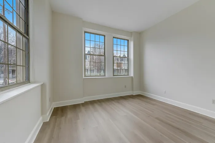 Empty bedroom at Franklin Manor Apartments, West Reading PA, with 3 windows, gray walls, and wood-look floors.