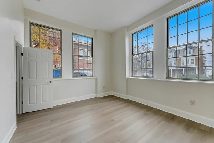 Empty bedroom at Franklin Manor Apartments with 4 windows, gray walls, and wood-look floors.