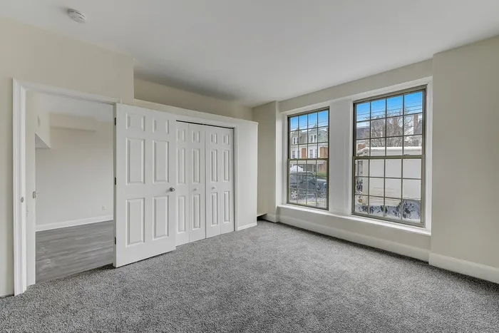 Empty bedroom with gray carpet, closet, and 2 large windows at Franklin Manor.