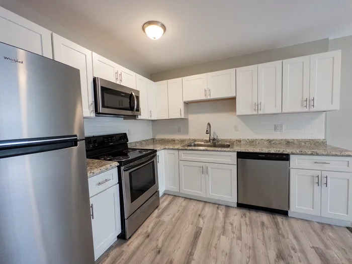Kitchen at 405 at Main Apartments with white cabinets, stainless appliances, granite counters, vinyl plank flooring.