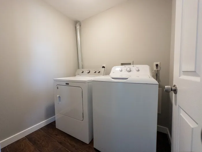 Side-by-side white washer and dryer in a compact laundry room at 405 at Main Apartments.