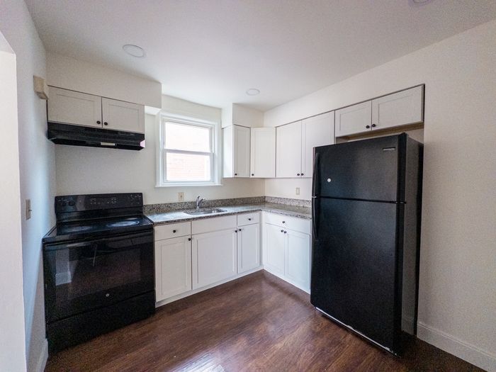 white kitchen with black fridge and oven, wood floor