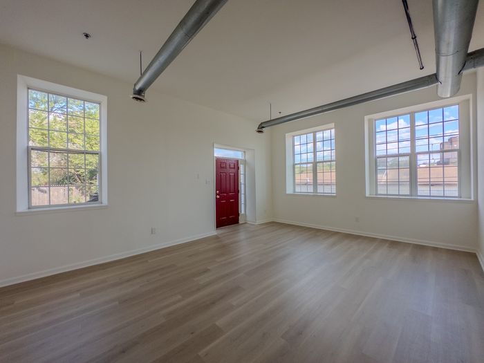 apartment interior, large windows and red front door, exposed air vents and vinyl plank flooring, white walls and trim