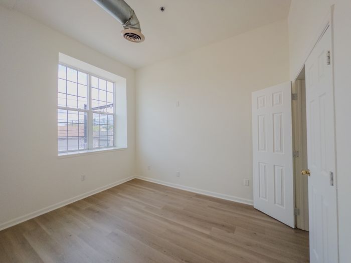 secondary bedroom, tall window, vinyl plank flooring, exposed air ducts and closet with double doors