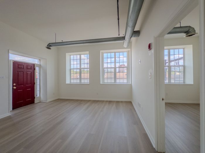 spacious living room and view into bedroom, large windows, red front door