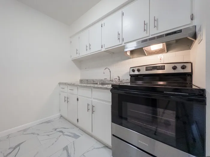 Kitchen at Woodland Manor Apartments with stainless range, white cabinets, granite-look counters, marble-look tile floor.