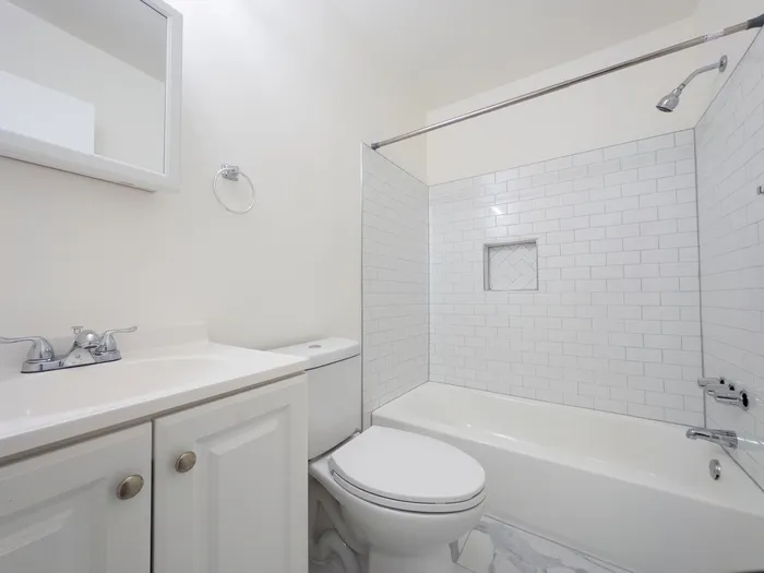 Bathroom with white vanity, toilet, and subway-tiled bathtub/shower at Woodland Manor Apartments in Morrisville, PA.