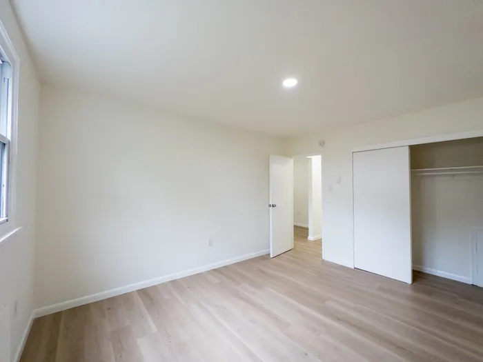 Bright empty bedroom with wood-look floors, open closet and window at Woodland Manor Apartments in Morrisville, PA.