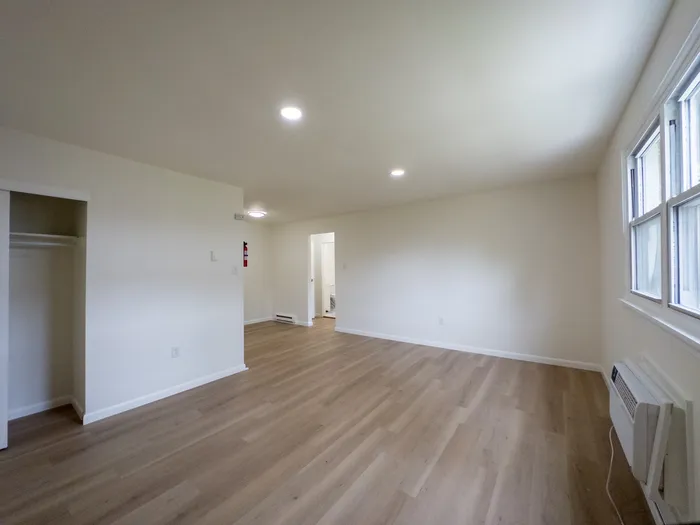 Spacious open living area at Woodland Manor Apartments with light wood floors, closet, windows, and wall air conditioner.