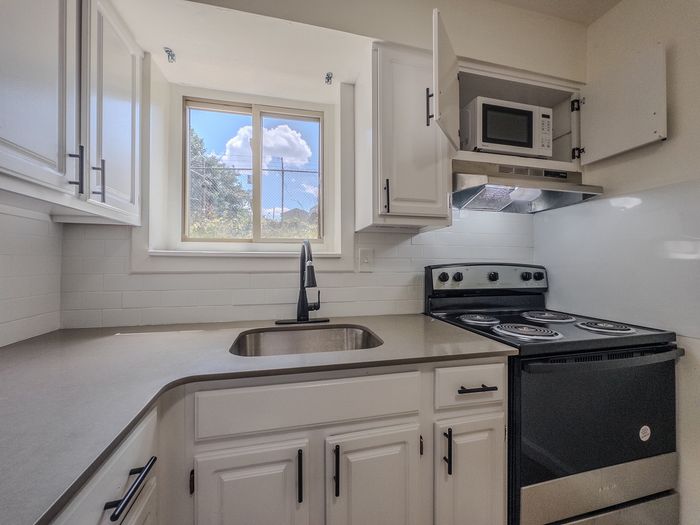 renovated kitchen with new microwave and oven, window over sink, stone countertops and white cabinets
