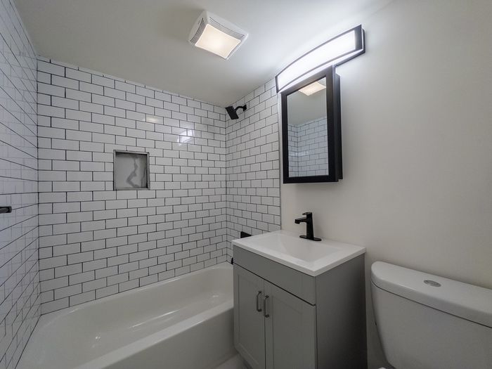 modern bathroom with subway tile shower including built in shelf, black accents, vanity sink