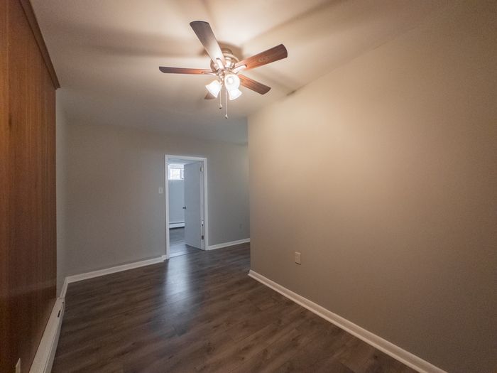 apartment room with ceiling fan and lights, vinyl flooring, doorway leading to bedroom with window
