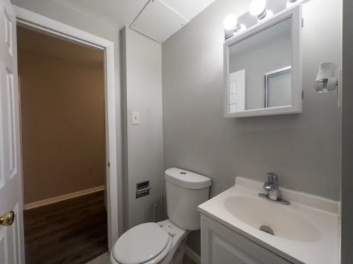 apartment bathroom, bright lights, vanity sink, energy efficient toilet, doorway leading to hall
