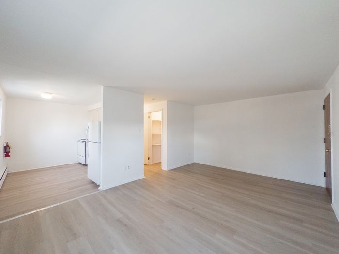 apartment living room with vinyl plank flooring, looking towards open kitchen and hallway with large walk-in closet