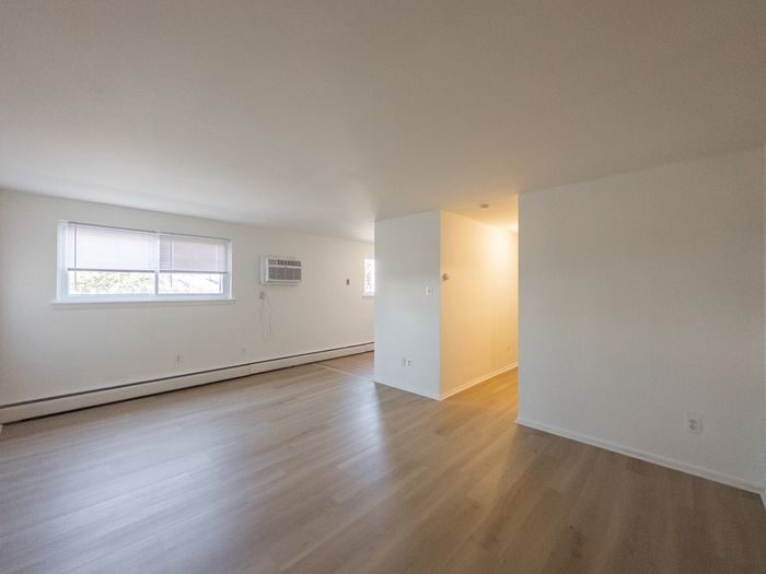 view from corner of living room, facing large window, air conditioner, hallway with lights, vinyl plank flooring