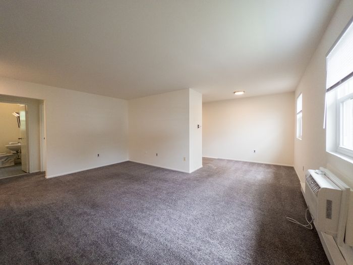 Spacious carpeted living room with window AC and a bathroom doorway in Laureldale, PA.