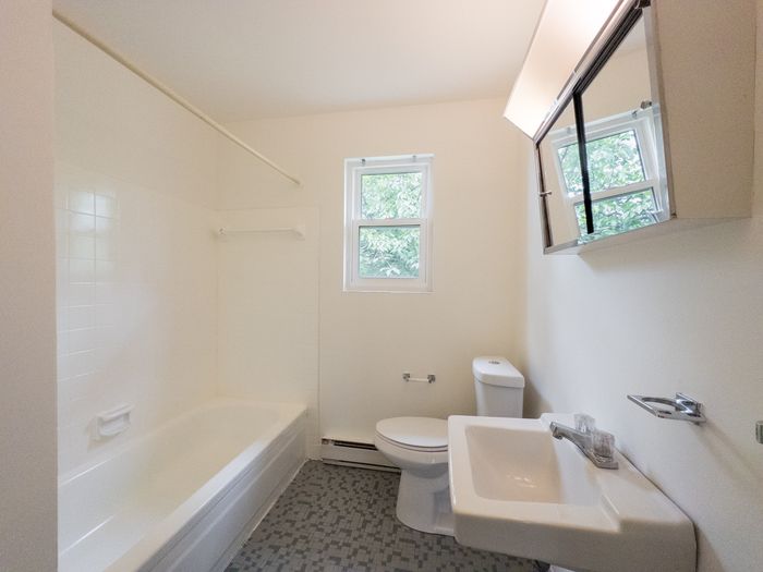 Bright bathroom at The Cloverleaf apartments in Laureldale, PA with tub, sink, toilet, and mirrored cabinet.