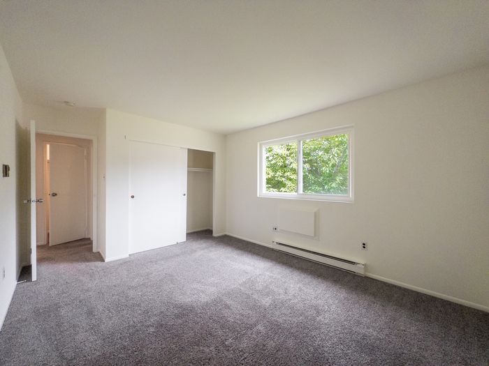 Bright empty bedroom with gray carpet, sliding-closet doors and window at The Cloverleaf apartments in Laureldale, PA.