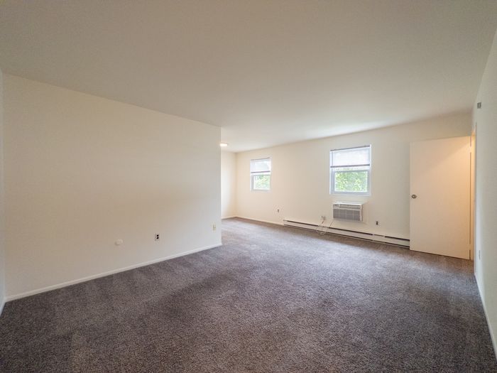 The Cloverleaf Apartments in Laureldale, PA, spacious empty carpeted living room with two windows and a wall air conditioner.