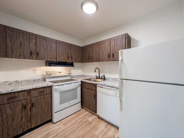 Kitchen at The Cloverleaf, Apartments with wood cabinets, white appliances, marble-look countertops.