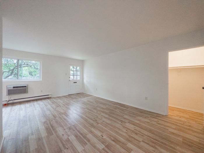 Empty living room with laminate floors, window AC, entry door, and open closet at The Cloverleaf in Laureldale, PA.