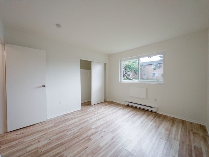 Unfurnished bedroom at The Cloverleaf Apartments in Laureldale, PA with sliding closet, large window, and wood-look flooring.