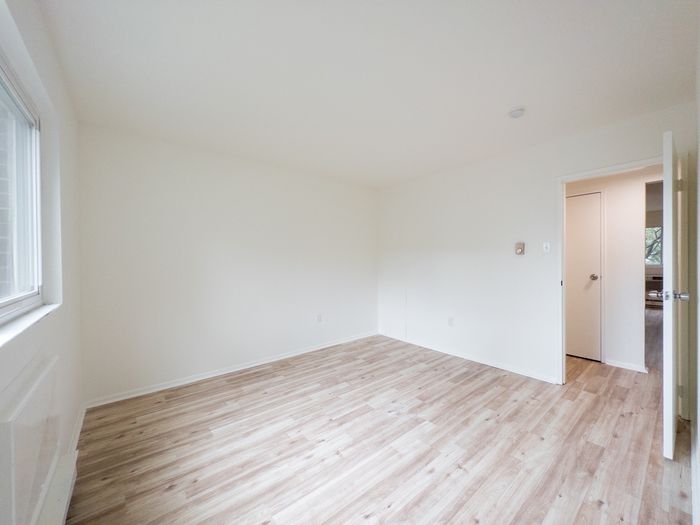 Bright empty room with wood-look flooring, white walls, window and open door.