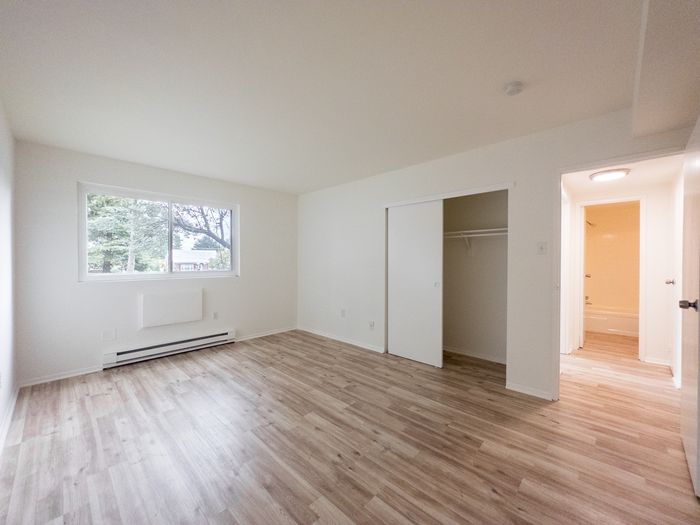 Bright vacant bedroom with wood-look floors, large window and open closet at The Cloverleaf, Apartments in Laureldale, PA.