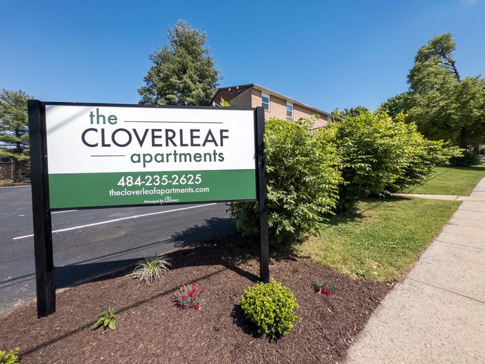 Sign for The Cloverleaf apartments by landscaped entrance in Laureldale, PA.