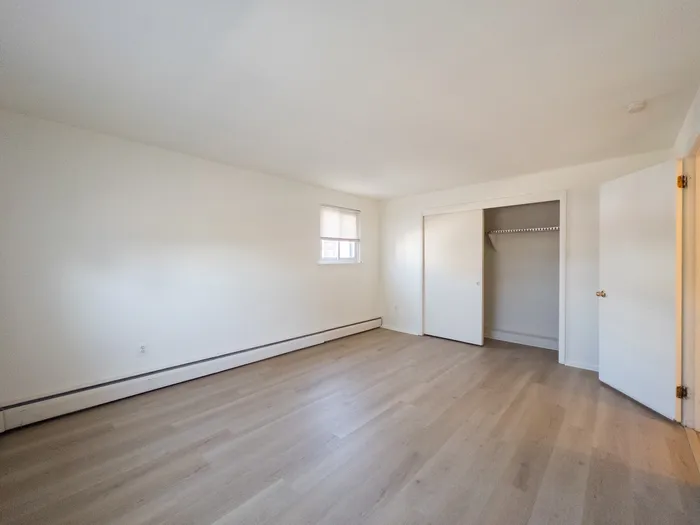apartment bedroom with wood panel floor, window, closet