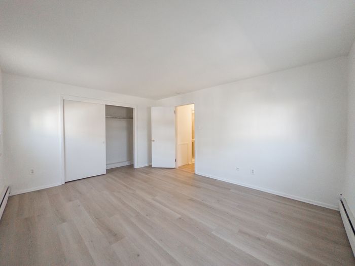 apartment bedroom with wood panel floor, closet, door leading to hallway, baseboard heating