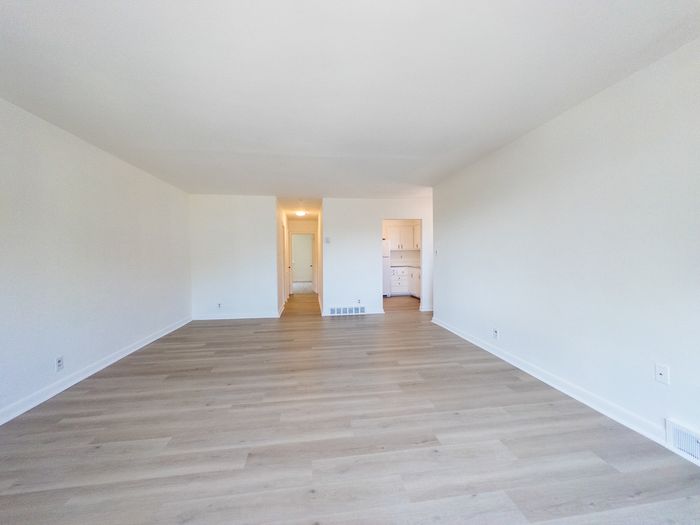 spacious apartment living room, wood flooring, storage closet, renovated apartment, doorways to kitchen and hallway