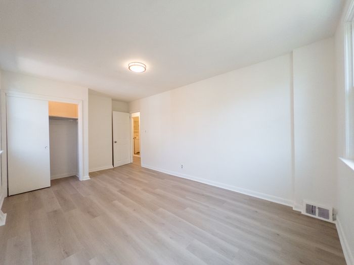 renovated apartment bedroom, wood panel floor, overhead light, closet with light, doorway to hall