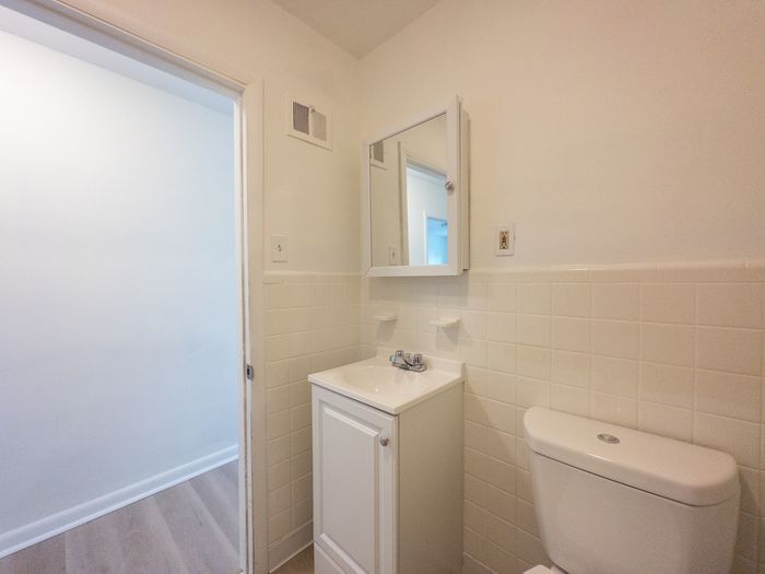 bathroom next to hallway, tile wall, vanity sink with medicine cabinet, energy efficient toilet