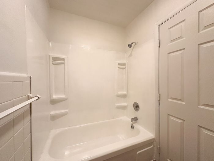 ceramic tub/shower combo, tile wall, door leading to hallway
