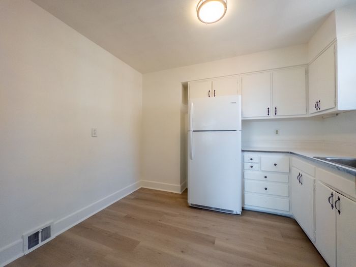 apartment kitchen with new wood floor, overhead light, white wood cabinets, refrigerator