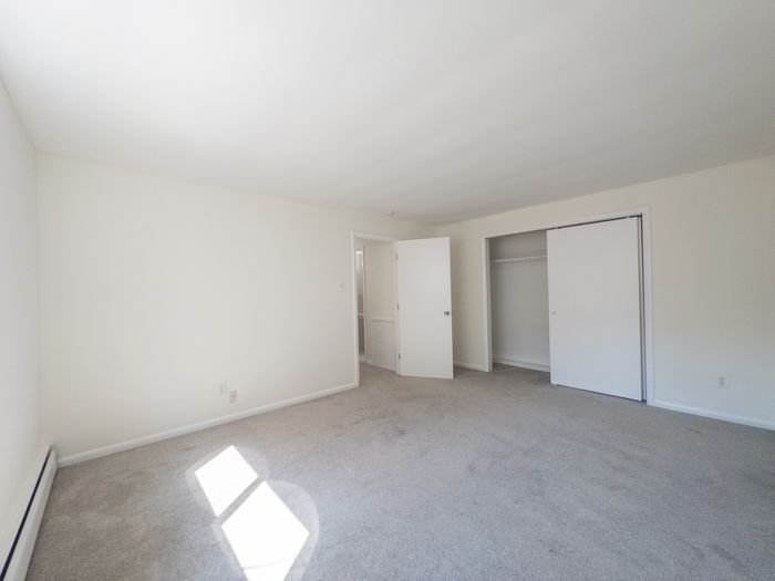 carpeted bedroom with long closet, door leading to hallway, natural light